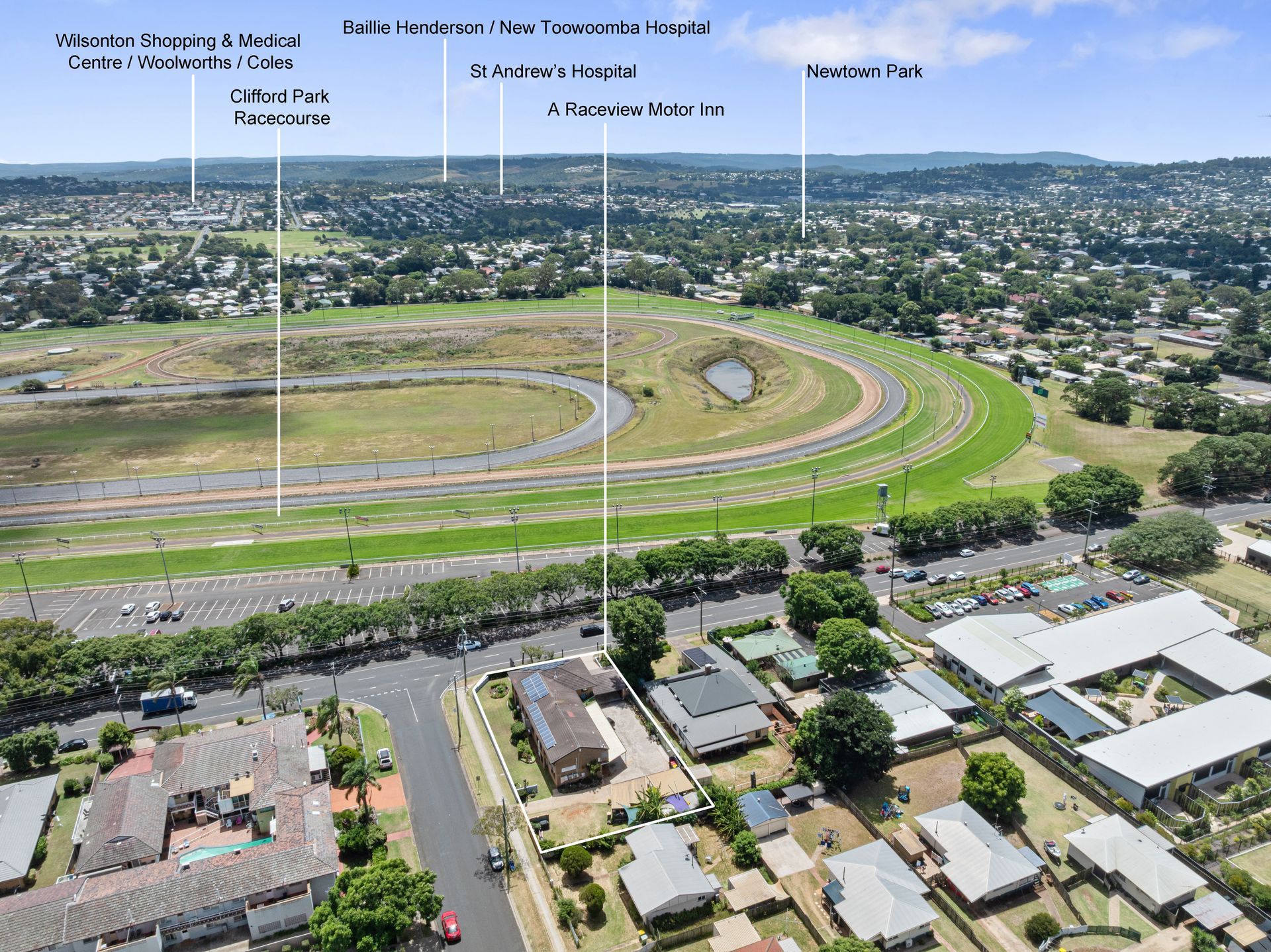 Aerial view of a racetrack oval amid a suburban neighborhood and cityscape.