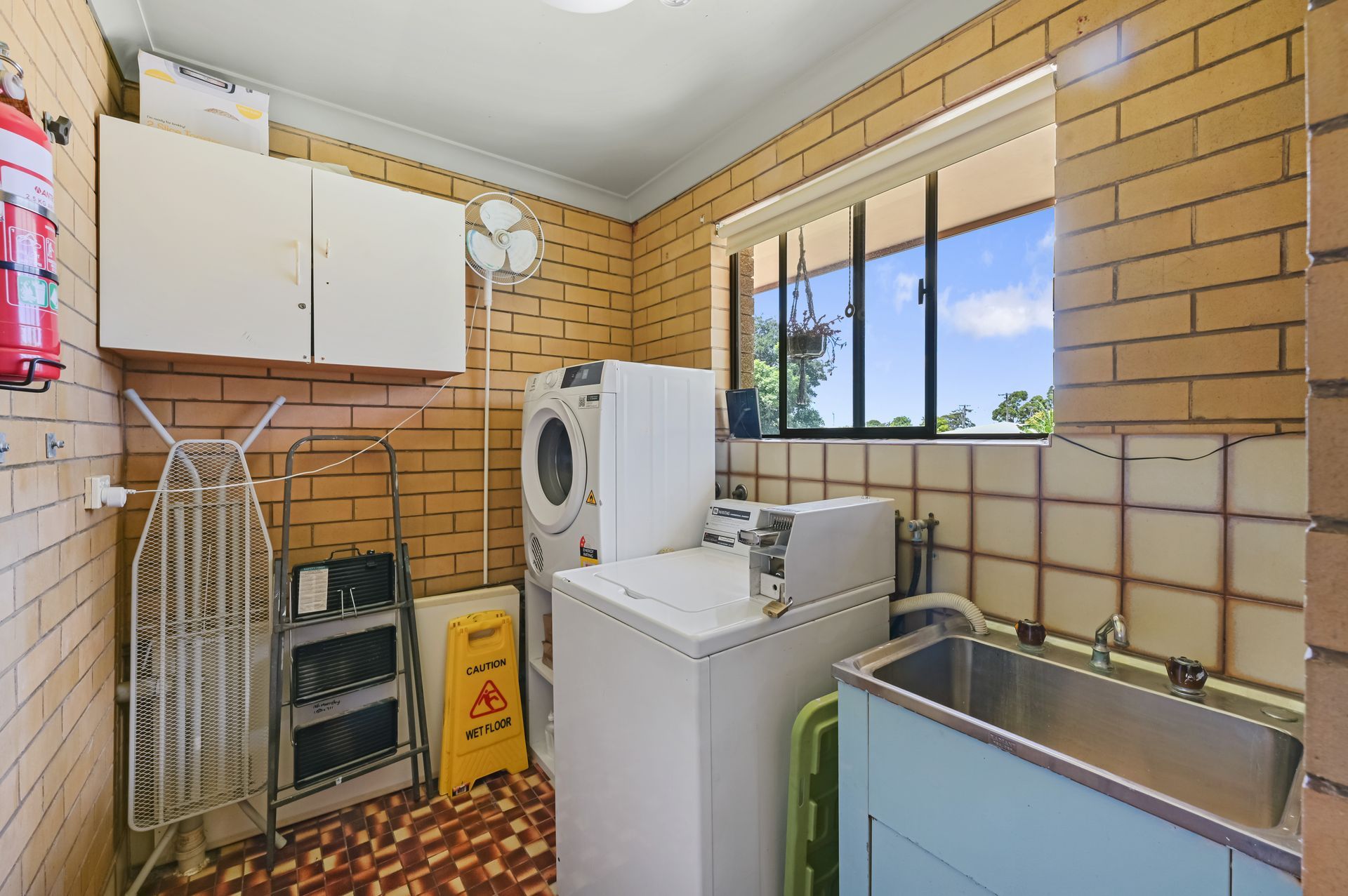 Laundry room with washer, dryer, sink, cabinets, and a window in a tiled space