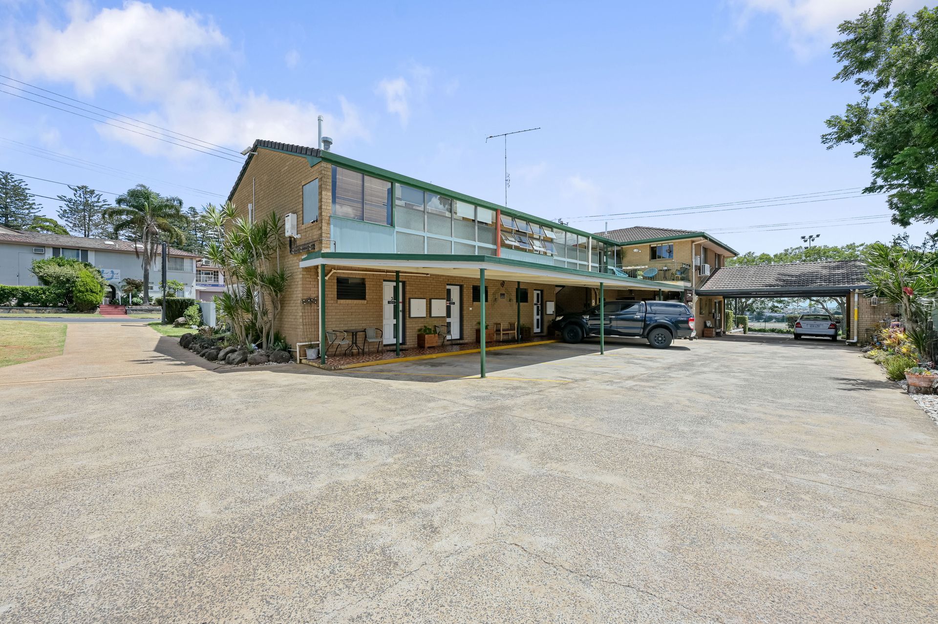 Two-story building with a covered porch and gravel parking area under a bright blue sky