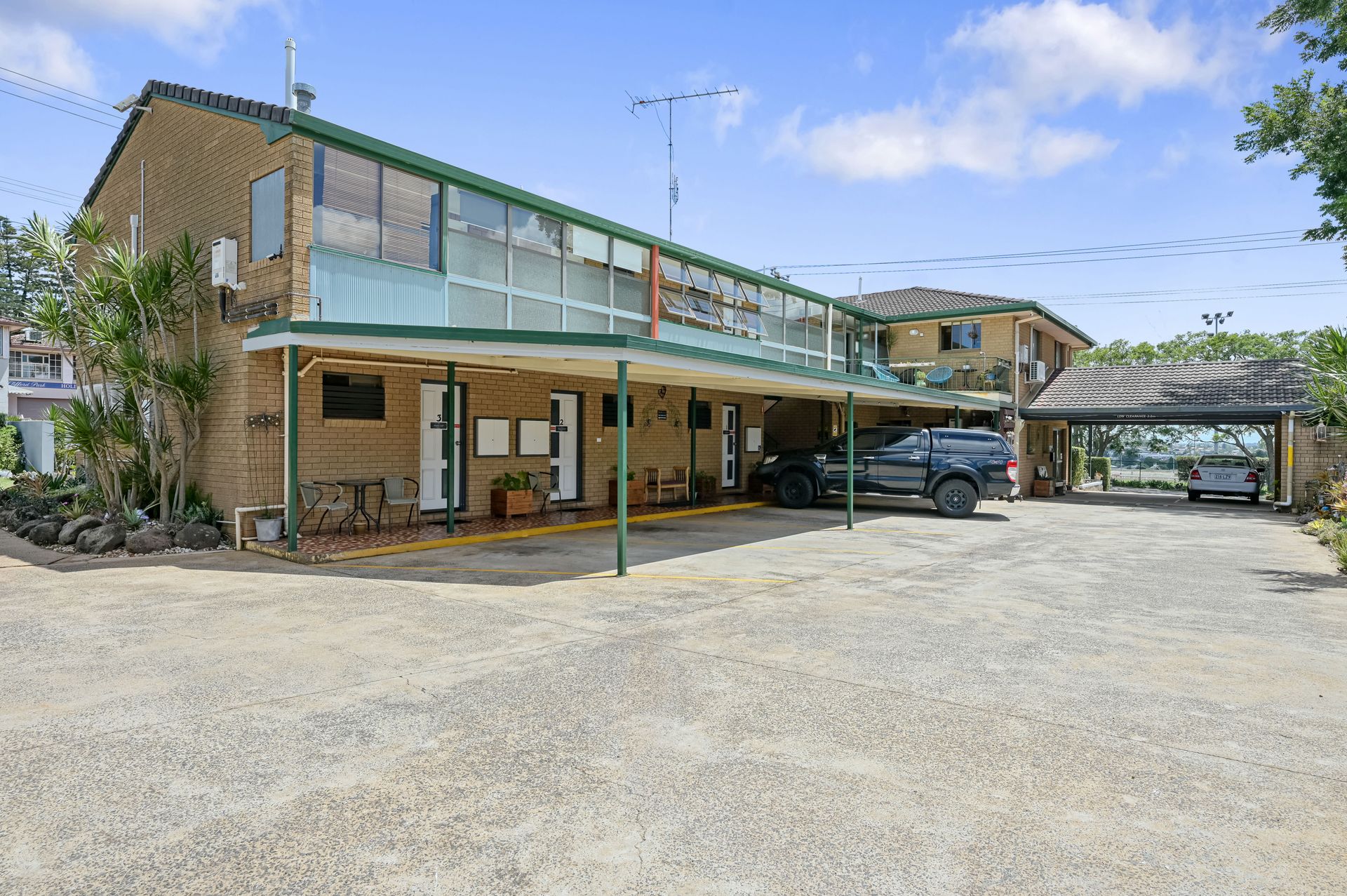 Modern two-story building with covered parking and gravel lot under a blue sky