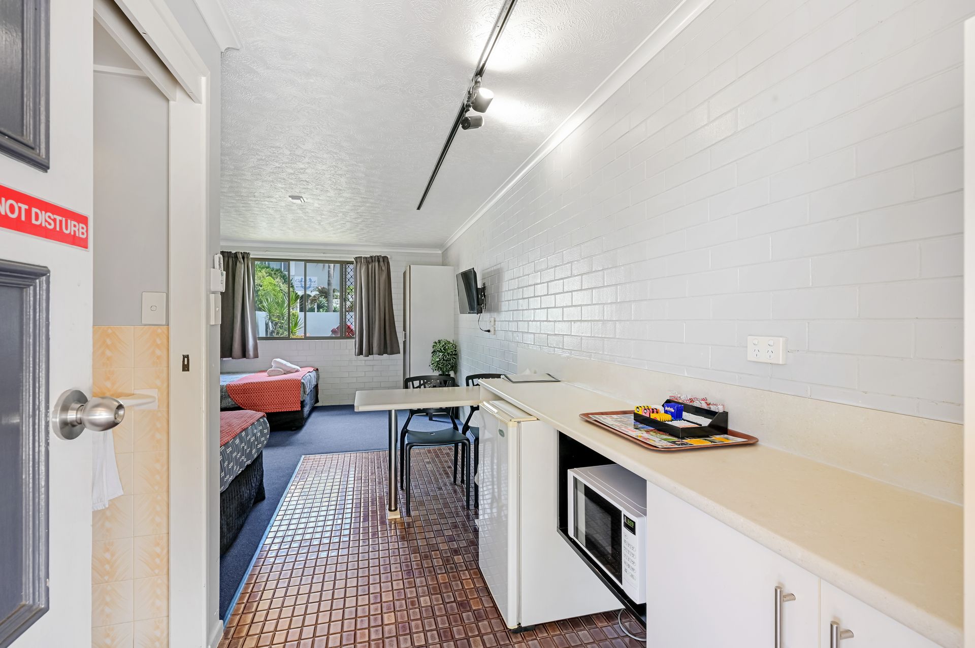 Narrow studio room with bed, table, kitchenette, white walls, and window view