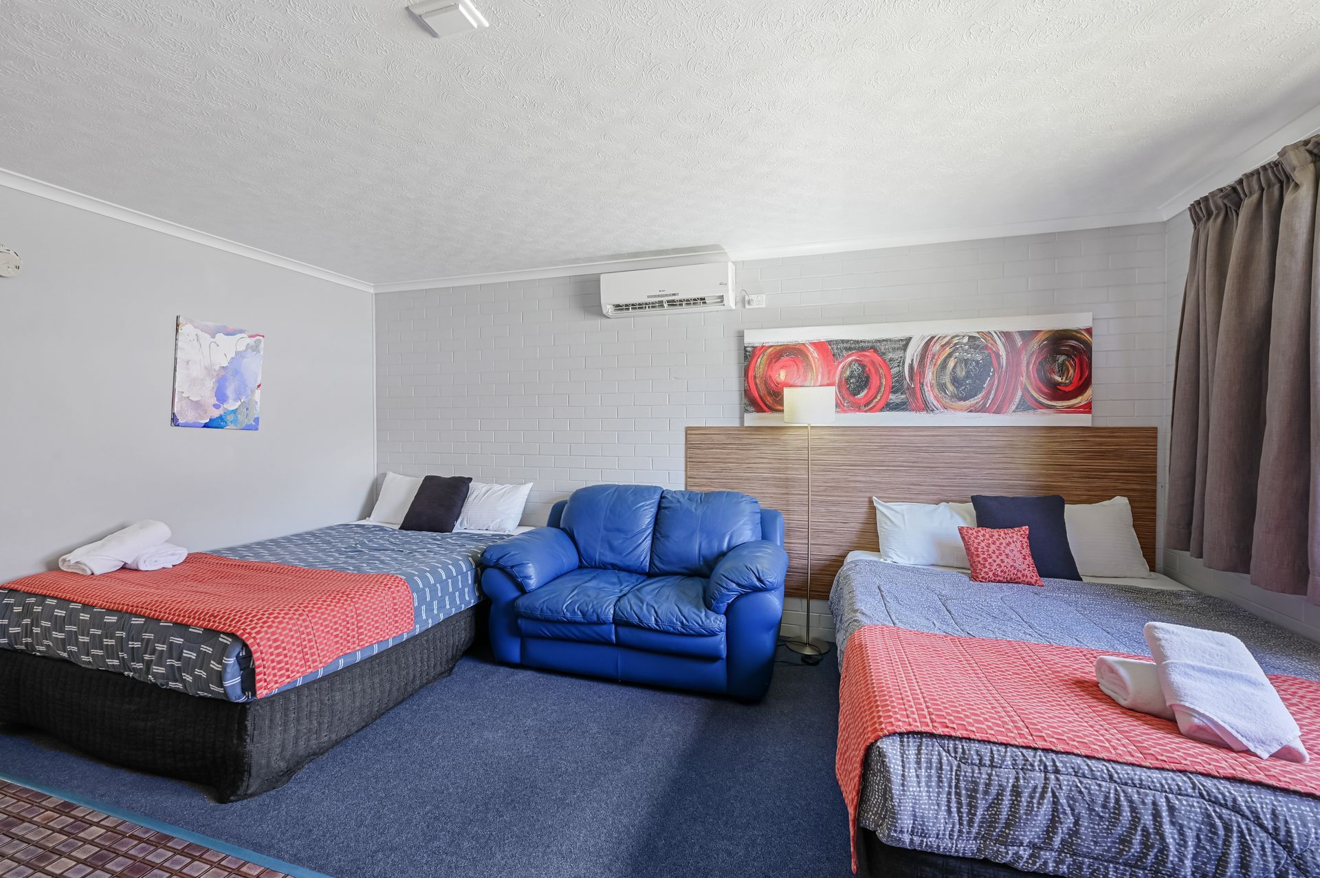 Hotel room with two beds, blue armchair, and wall art in a gray interior