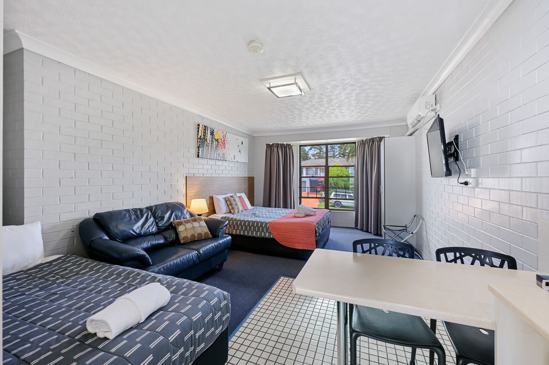 Bright living room with black sofas, red bedspread, white table, and glass doors to a balcony