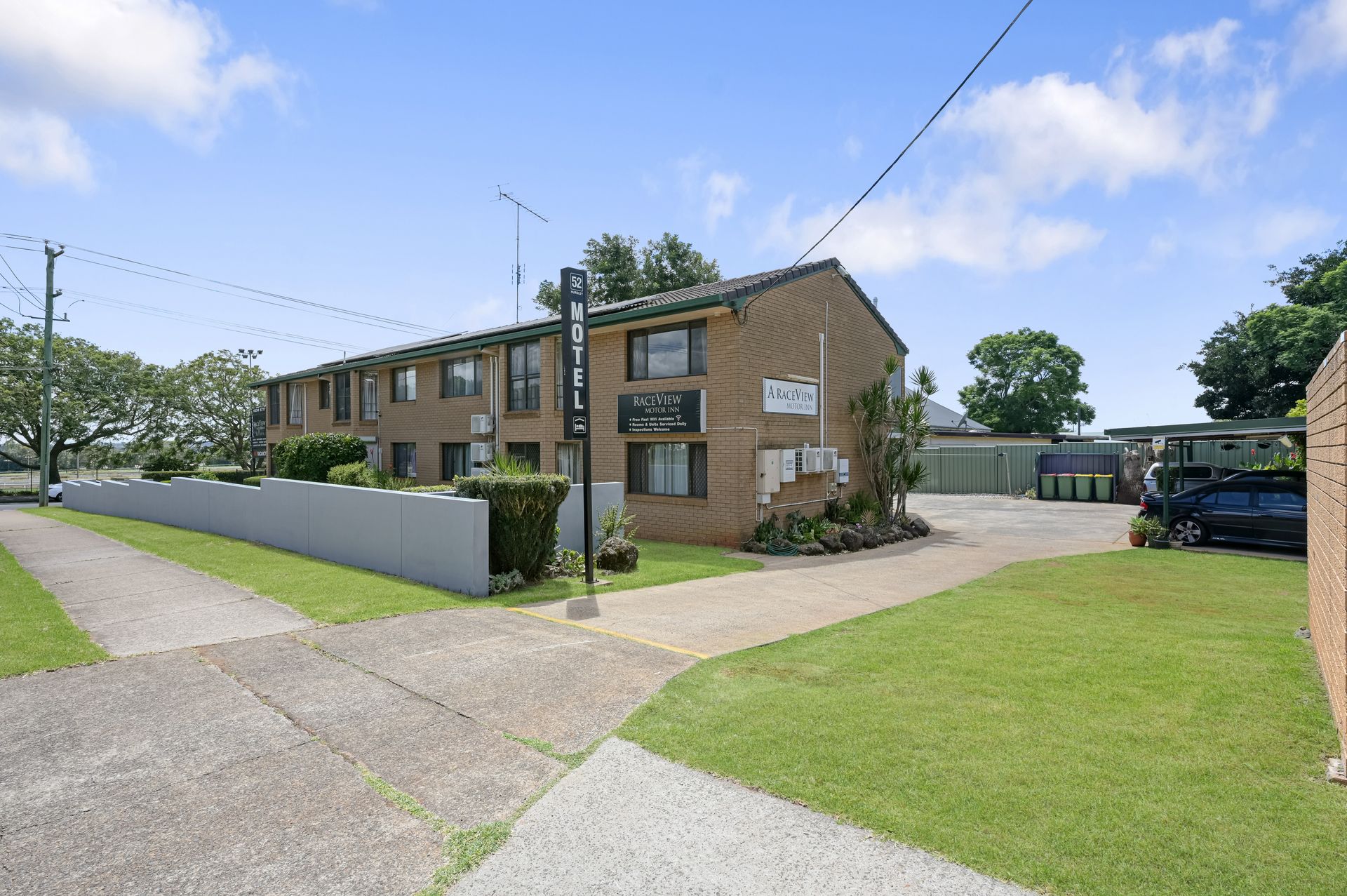 Brick apartment building with balconies beside a lawn and driveway on a sunny day