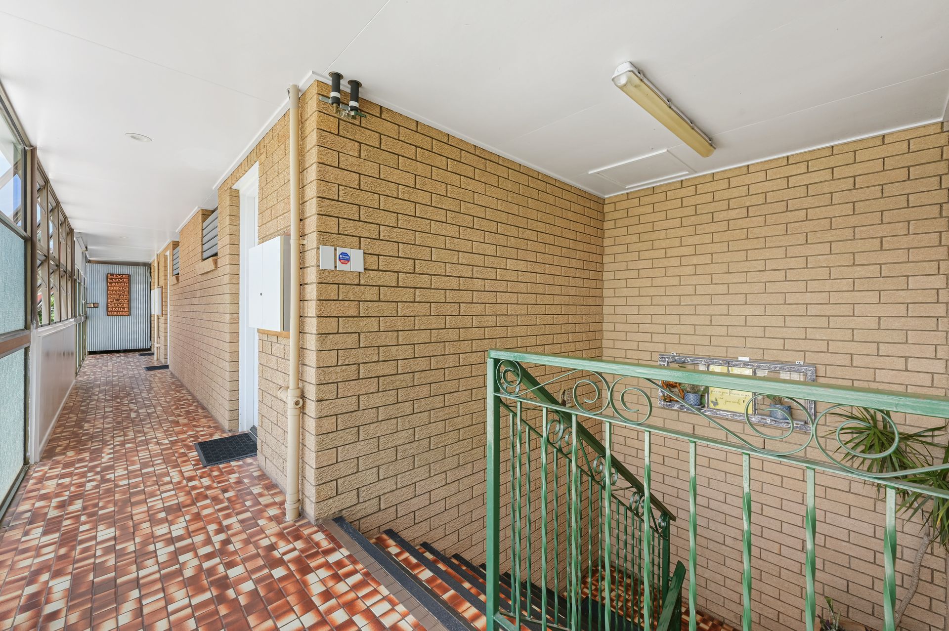 Apartment hallway with brick walls, red mosaic floor, and green stair railing