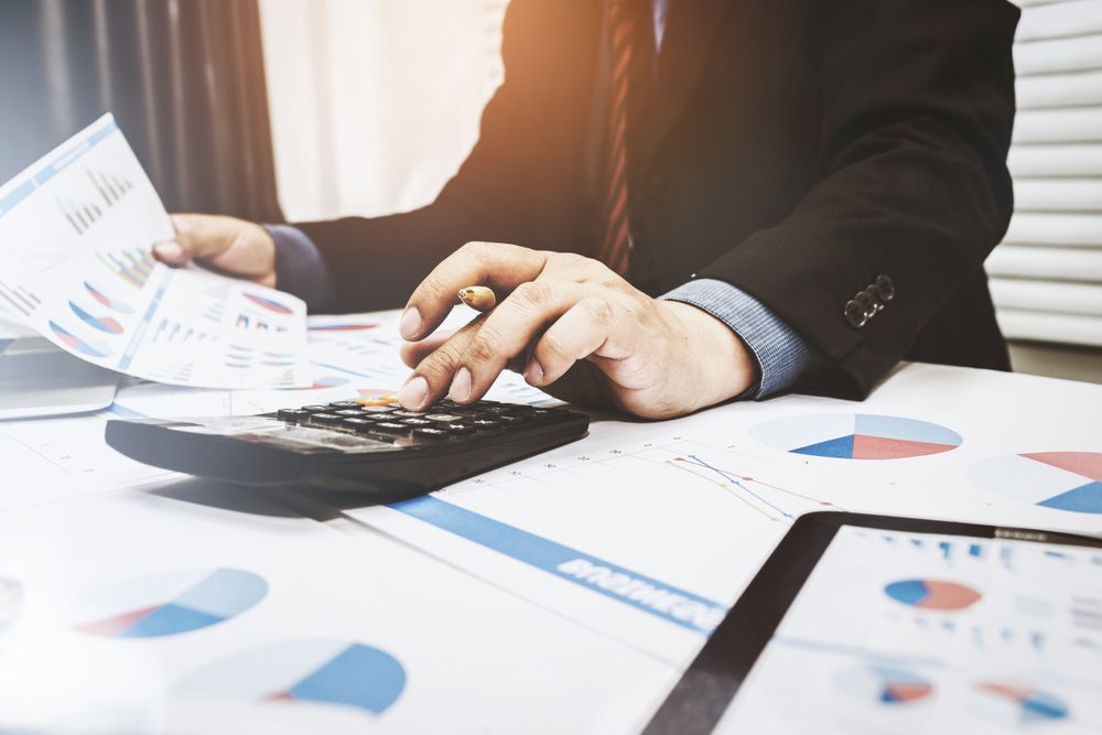 Person in Suit Using a Calculator, Surrounded by Financial Charts and a Tablet — Peterson Property Valuations In Sunshine Coast, QLD