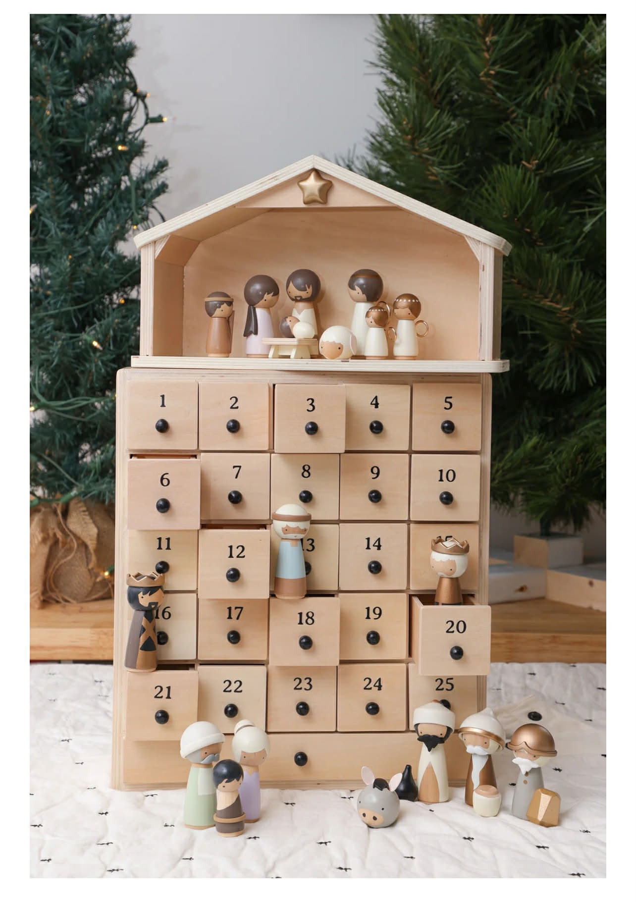 Wooden advent calendar shaped like a house, with small figurines and numbered drawers on a white surface.