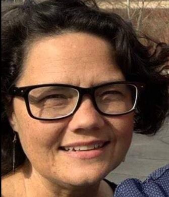 Smiling person with dark hair and black glasses outdoors in bright sunlight