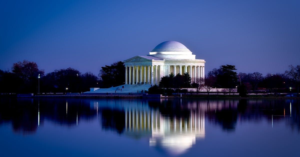 Illuminated Jefferson Memorial at dusk reflected in the calm Tidal Basin water.