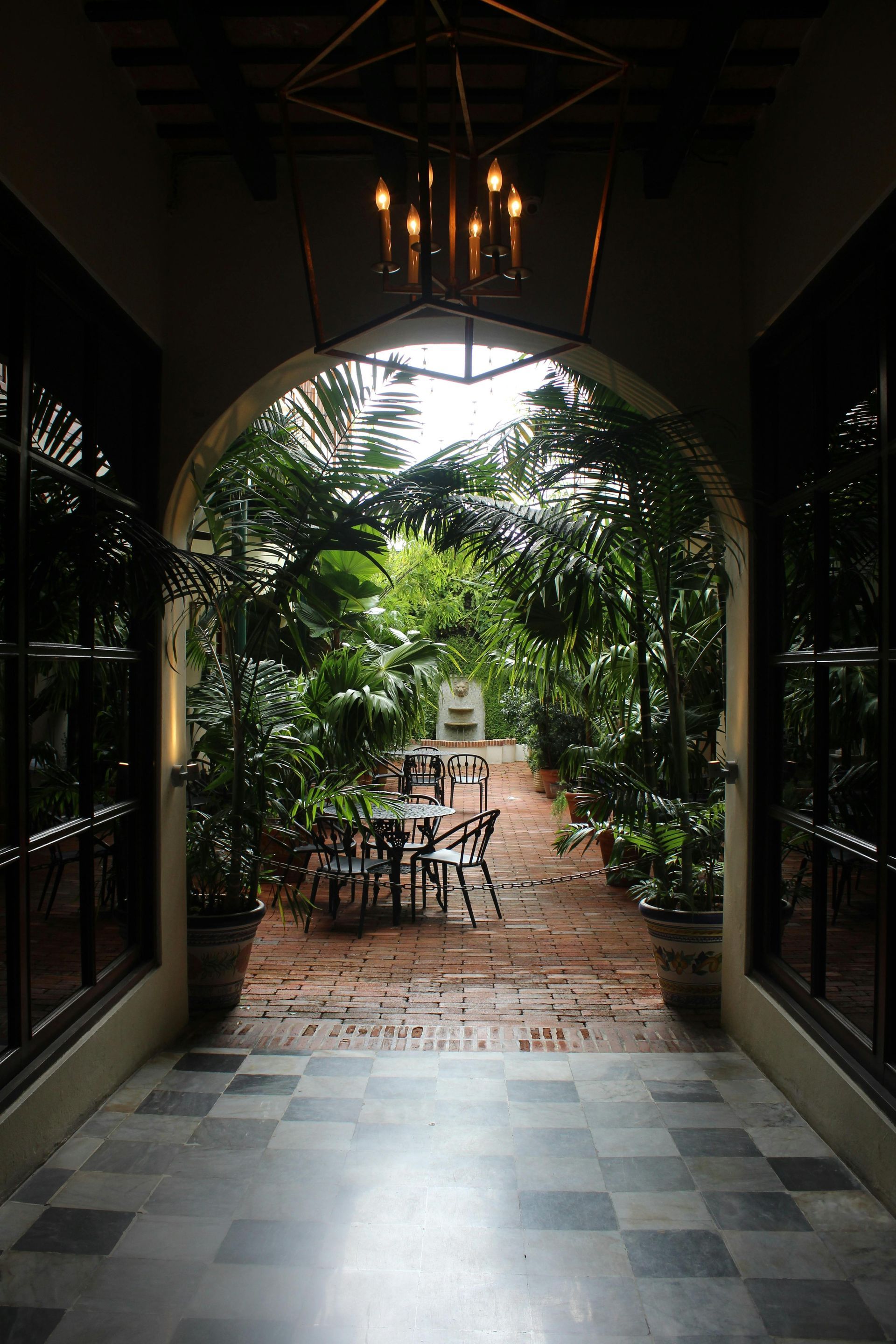 Arched walkway opening to a lush garden patio with tables, chairs, and hanging chandelier lights