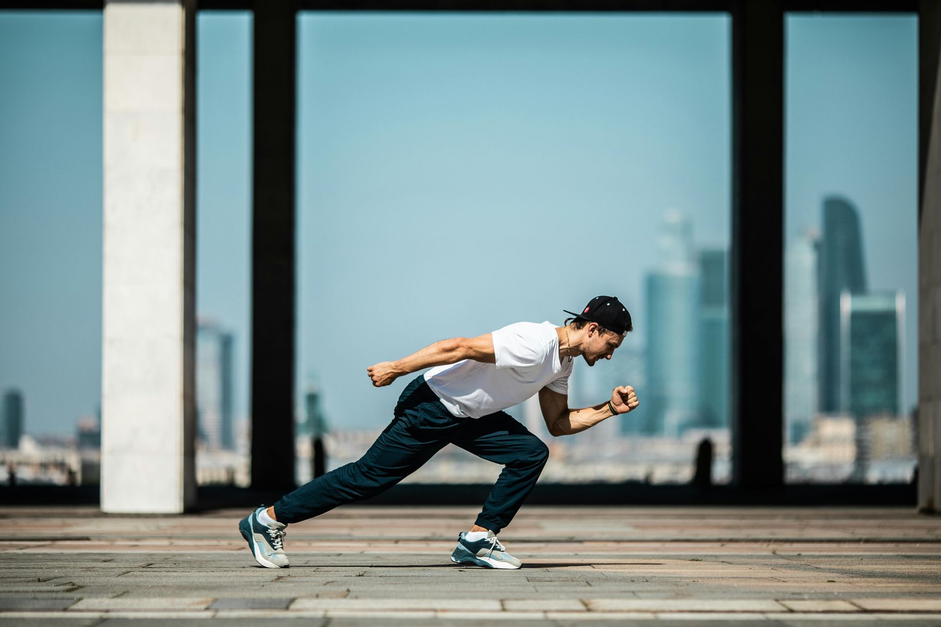 Runner in white shirt and jeans sprinting past large windows in an urban setting.