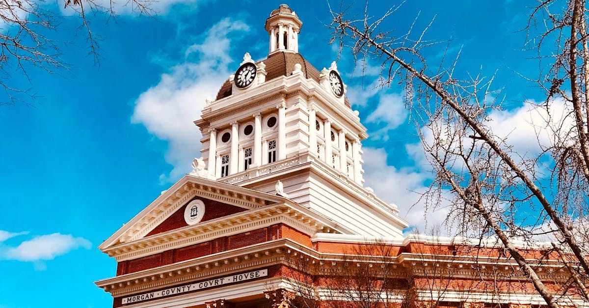 Historic clocktower under a bright blue sky with wispy clouds and bare tree branches in the foreground