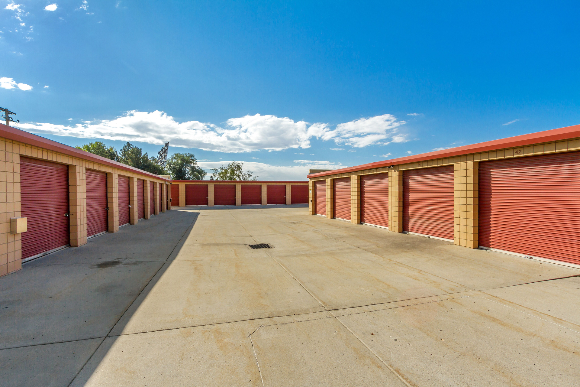 Rows of red storage units with a concrete drive under a blue sky.