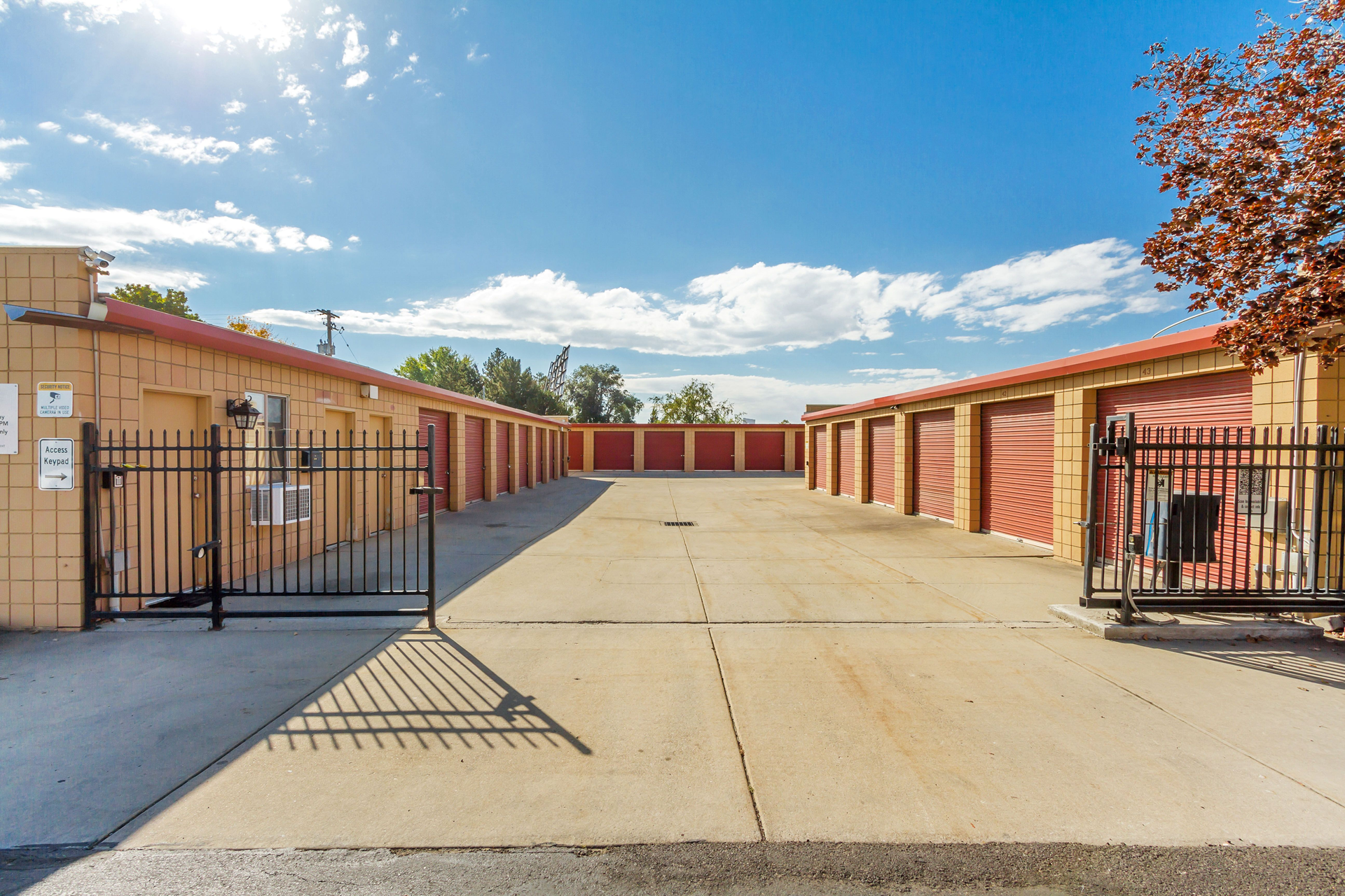 Storage units behind a black fence with red doors. Sunny day with blue sky.
