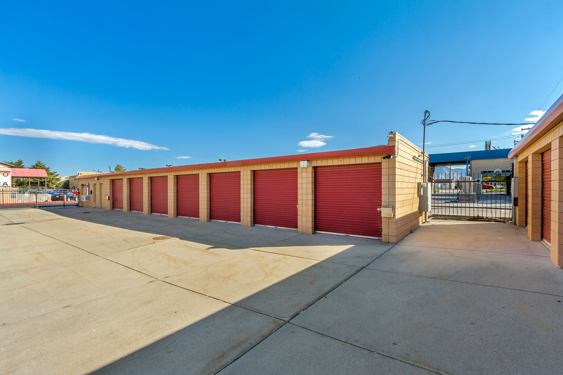 Storage units with red doors under a clear blue sky. Concrete lot with brick buildings.