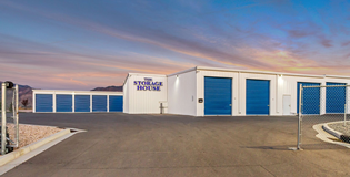Storage facility with blue doors and signage against a sunset sky.