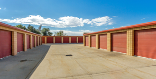 Storage units with red doors and tan brick trim, blue sky with clouds.