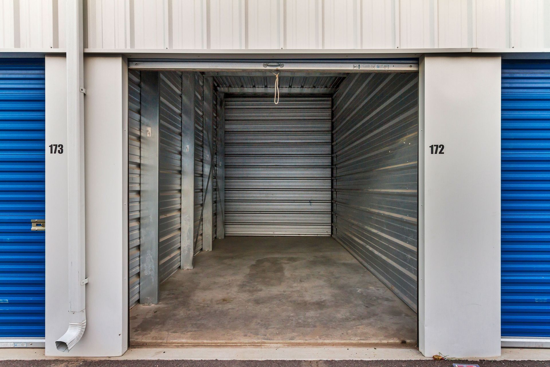 Empty storage unit with open metal door, blue doors on either side.