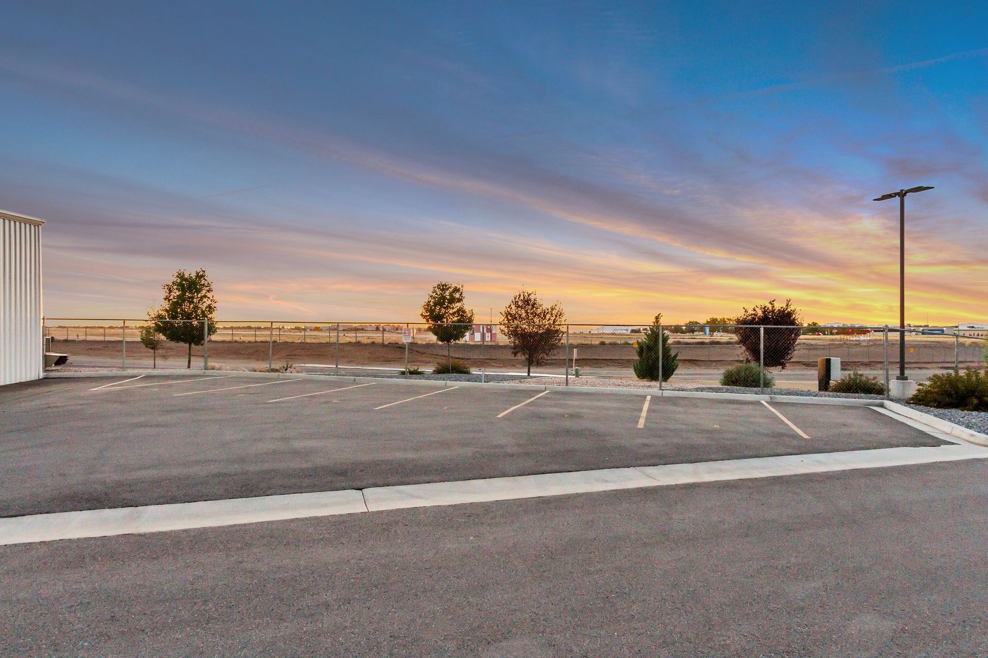 Empty parking lot with trees against a sunset sky.