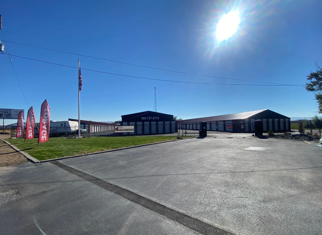Storage facility with a paved driveway, blue sky, and a bright sun.