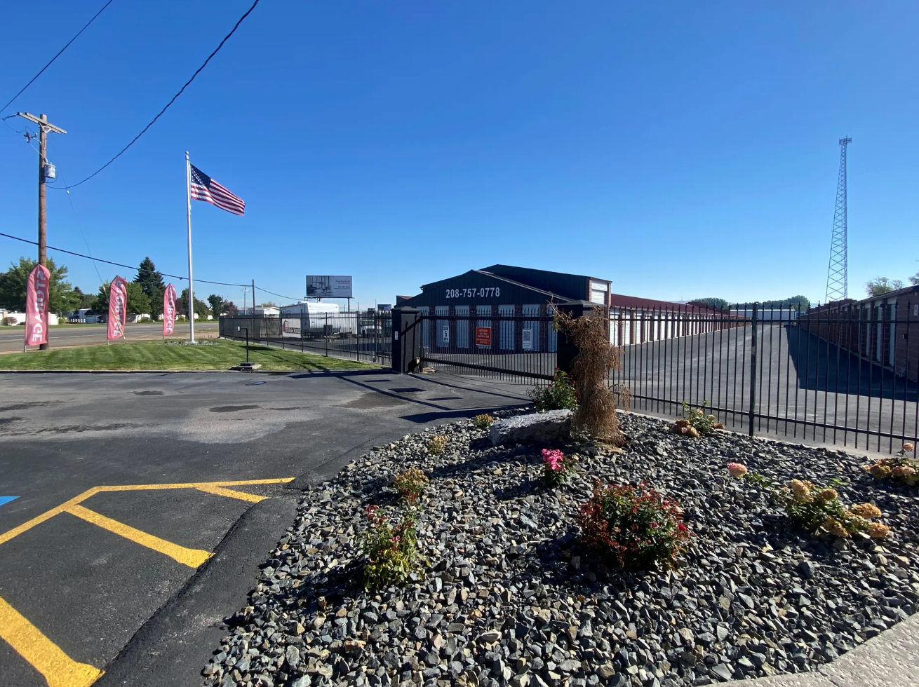Storage facility with black building, gate, and American flag. Blue sky, landscaping.