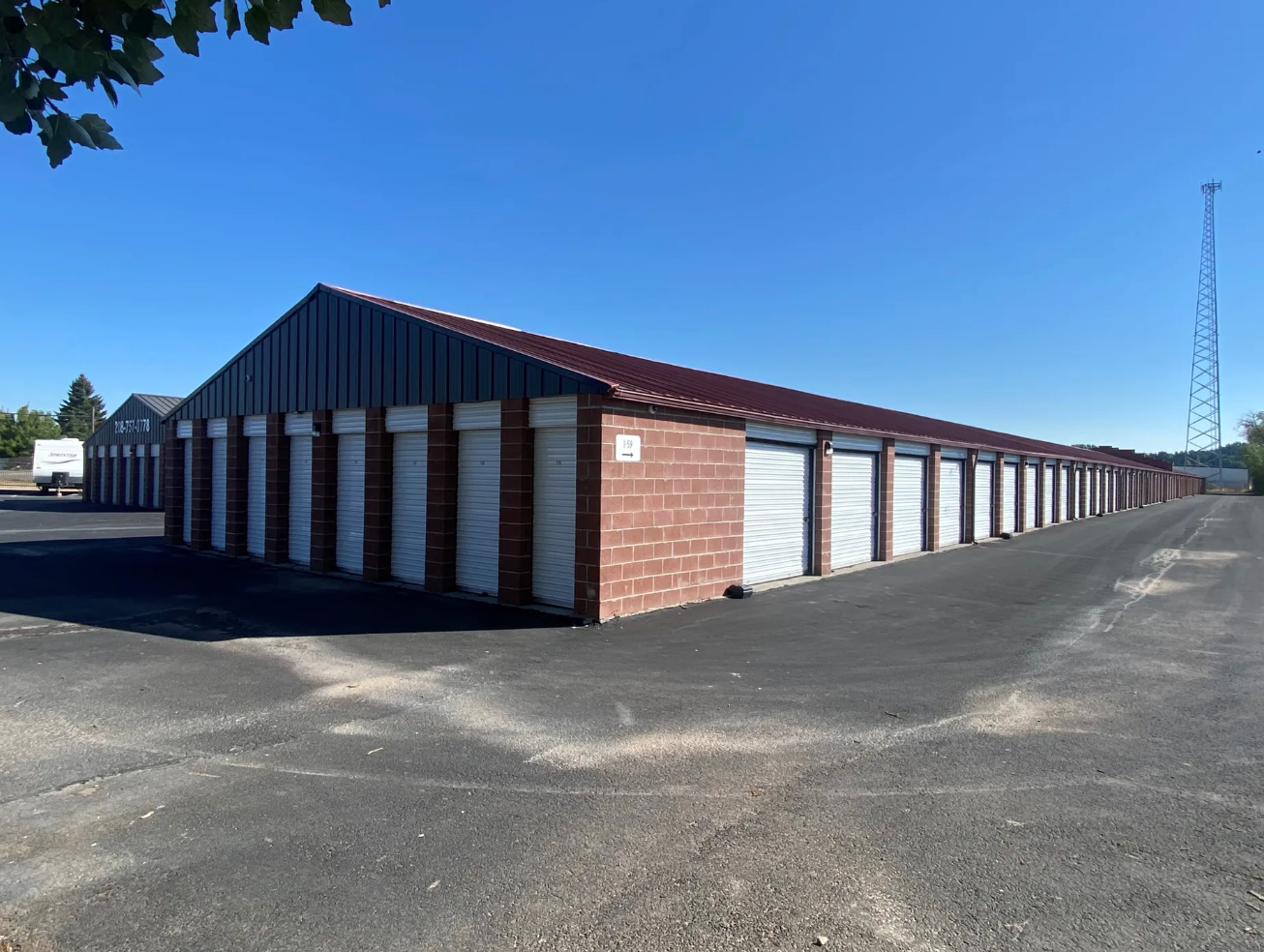 Row of storage units with red brick facade and metal doors under a blue sky.