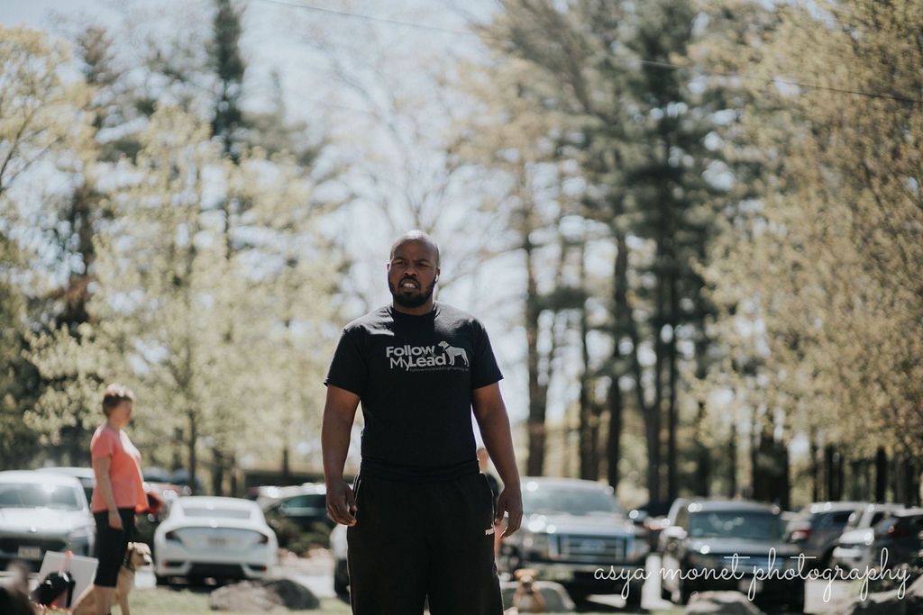 Man standing in a parking lot with cars and trees in the background, wearing a black T-shirt.