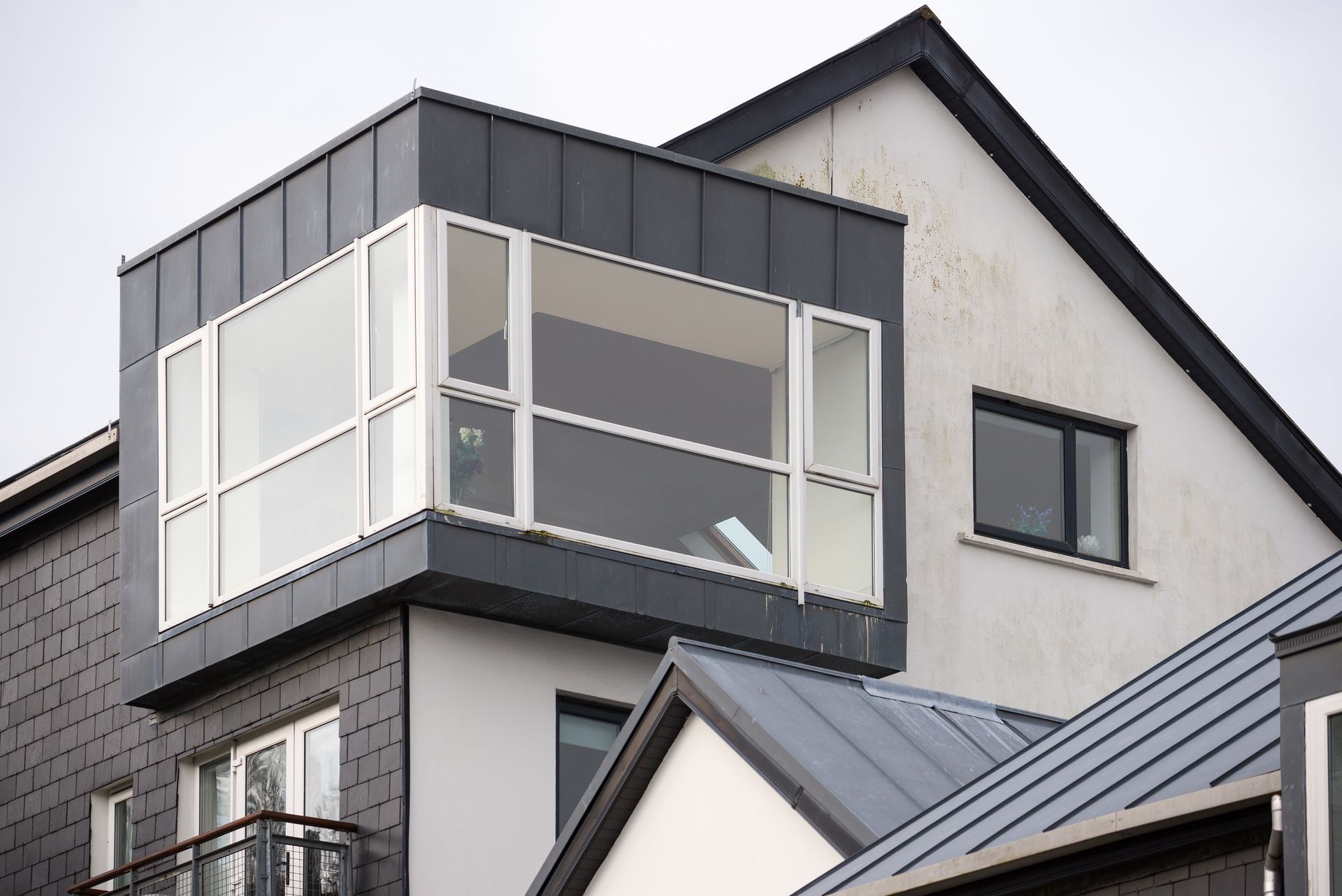 Modern house facade with a white enclosed balcony and gray roof panels Modern house facade with a white enclosed balcony and gray roof panels