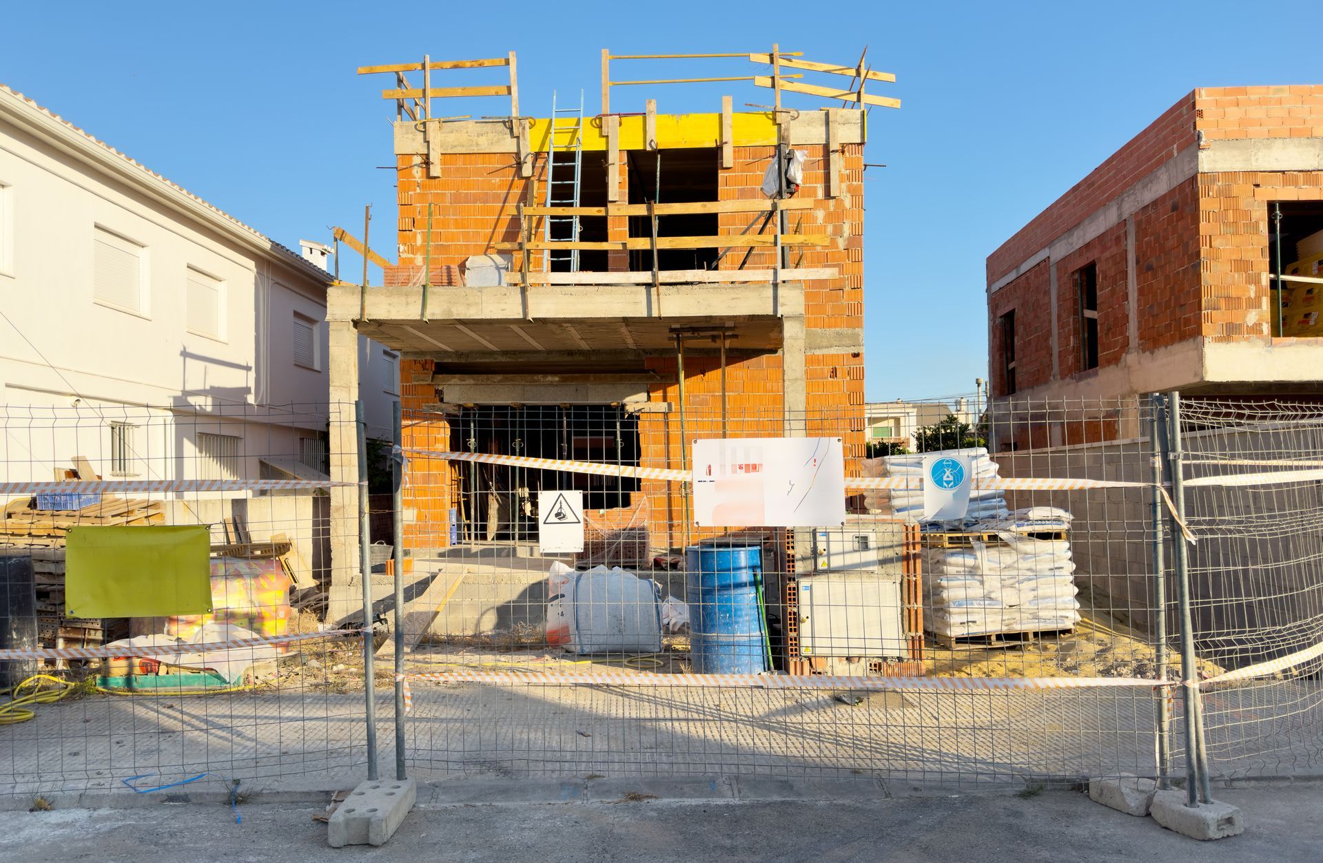 Construction site with a building under renovation, scaffolding, and fenced-off work area under a clear blue sky