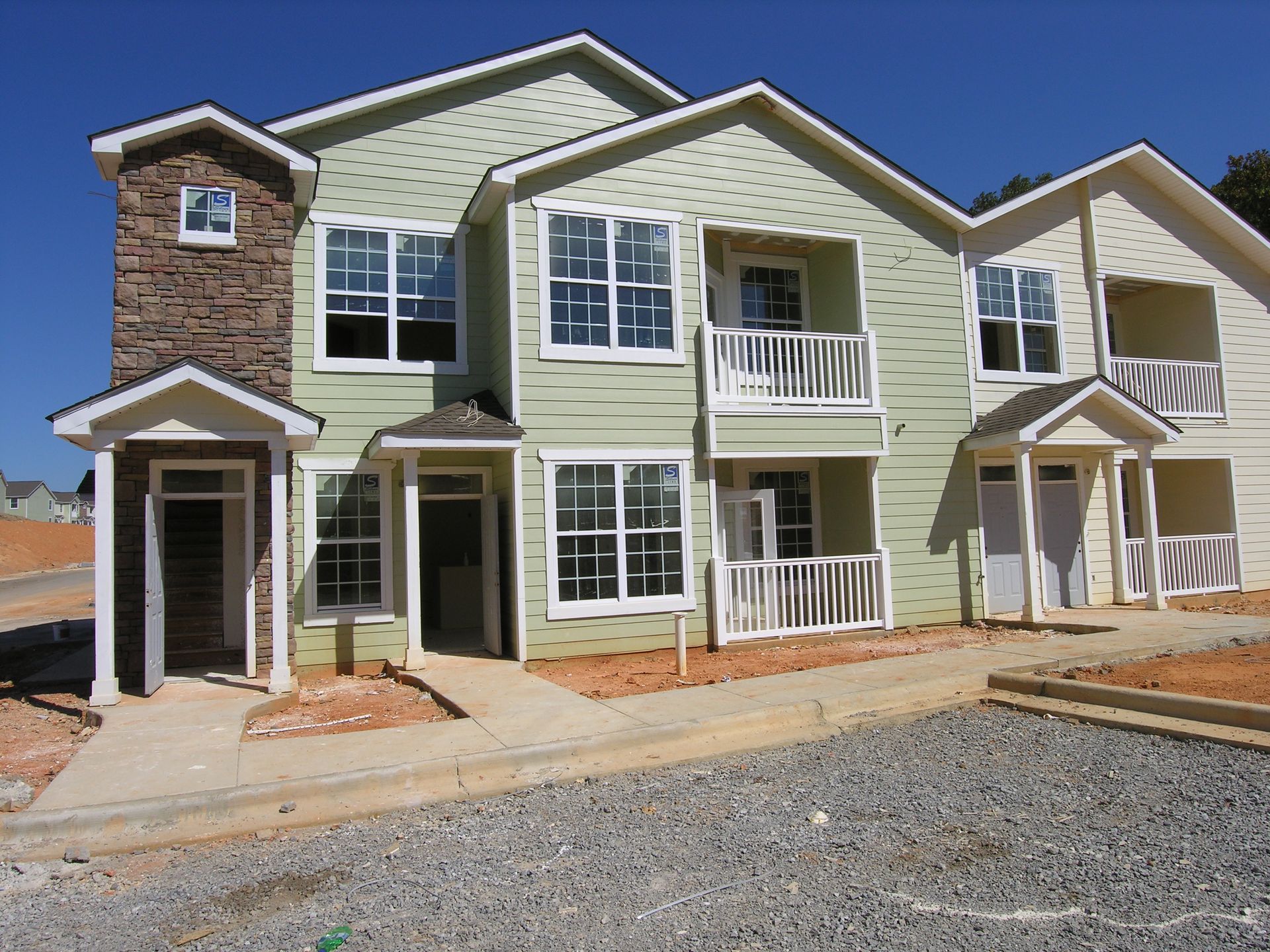 Row of beige townhouses with white trim and balconies, viewed from a gravel lot.