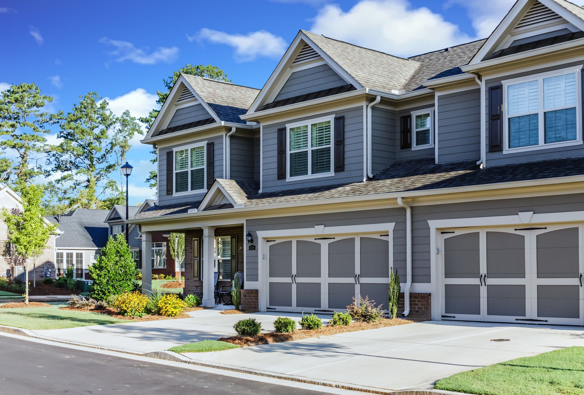 Suburban townhouse with attached garages, gray siding, and a blue sky on a sunny day