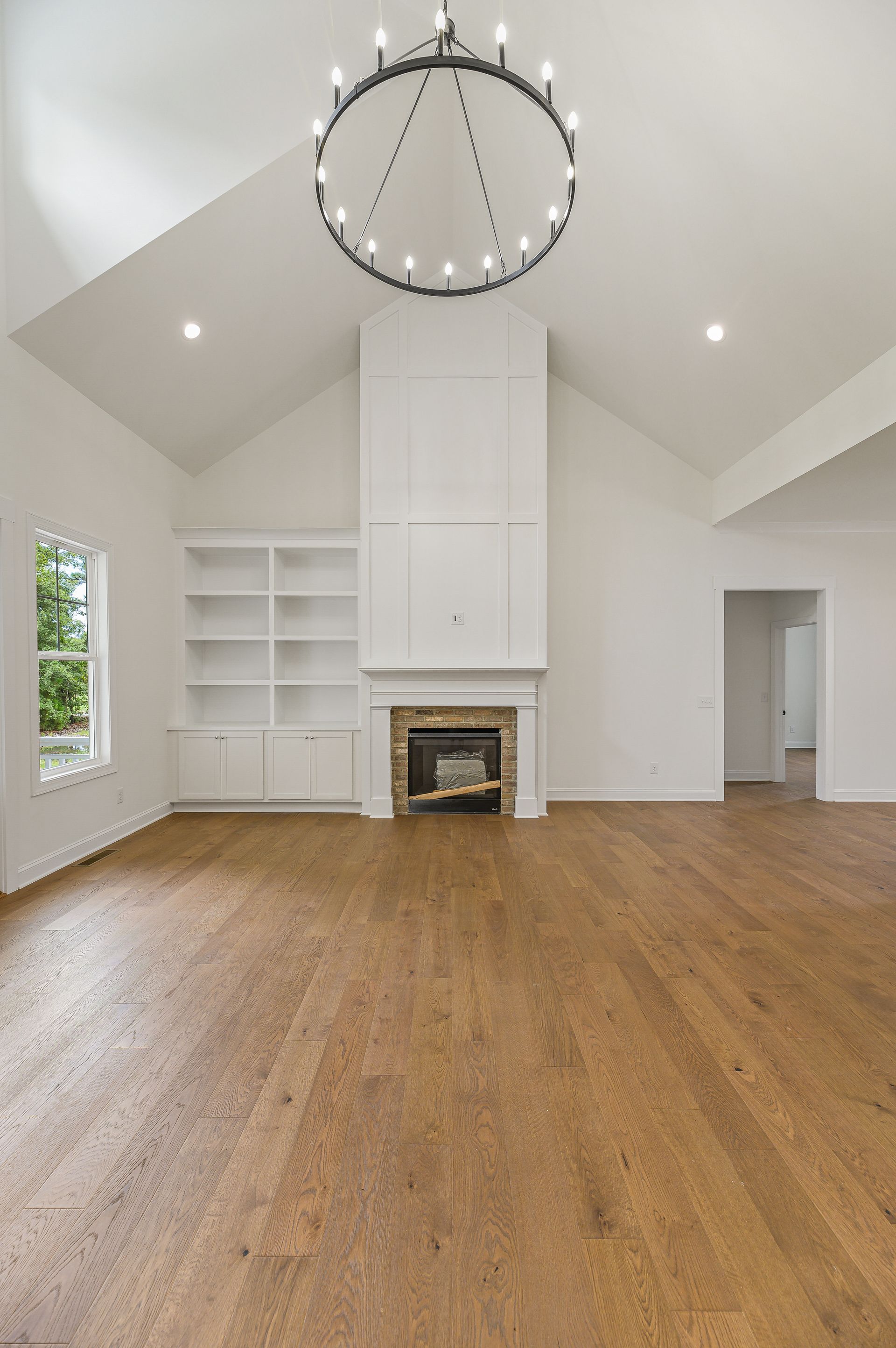 Bright empty living room with vaulted ceiling, fireplace, built-in shelves, and hardwood floors
