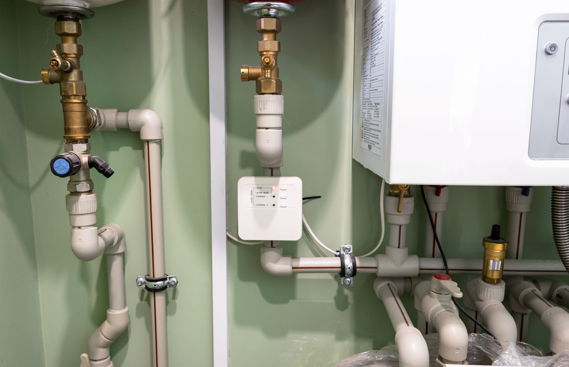 Boiler room plumbing with white pipes, valves, and wall-mounted heating equipment in a green utility room Boiler room plumbing with white pipes, valves, and wall-mounted heating equipment in a green utility room