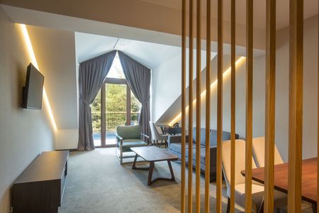 Modern hotel room with large window, lounge chairs, desk, bed, and warm ambient lighting