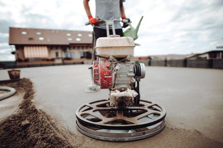Worker operating a concrete trowel on a freshly poured driveway near a building