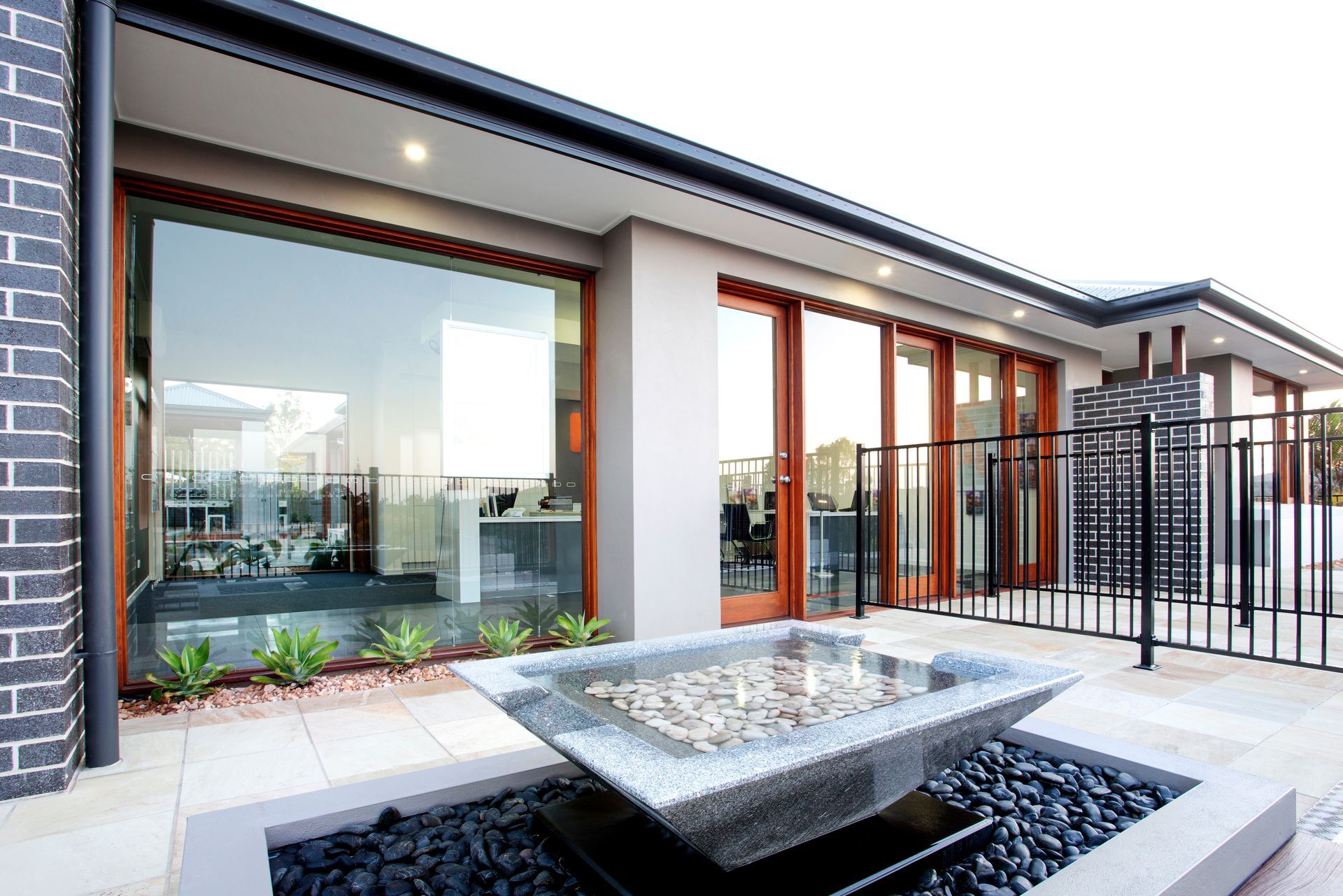 Modern house patio with large windows, black railing, and a stone fire pit in the foreground