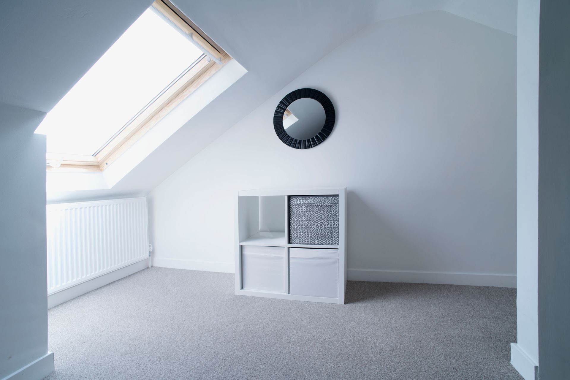 Empty attic room with skylight, radiator, small white storage unit, and round wall clock Empty attic room with skylight, radiator, small white storage unit, and round wall clock
