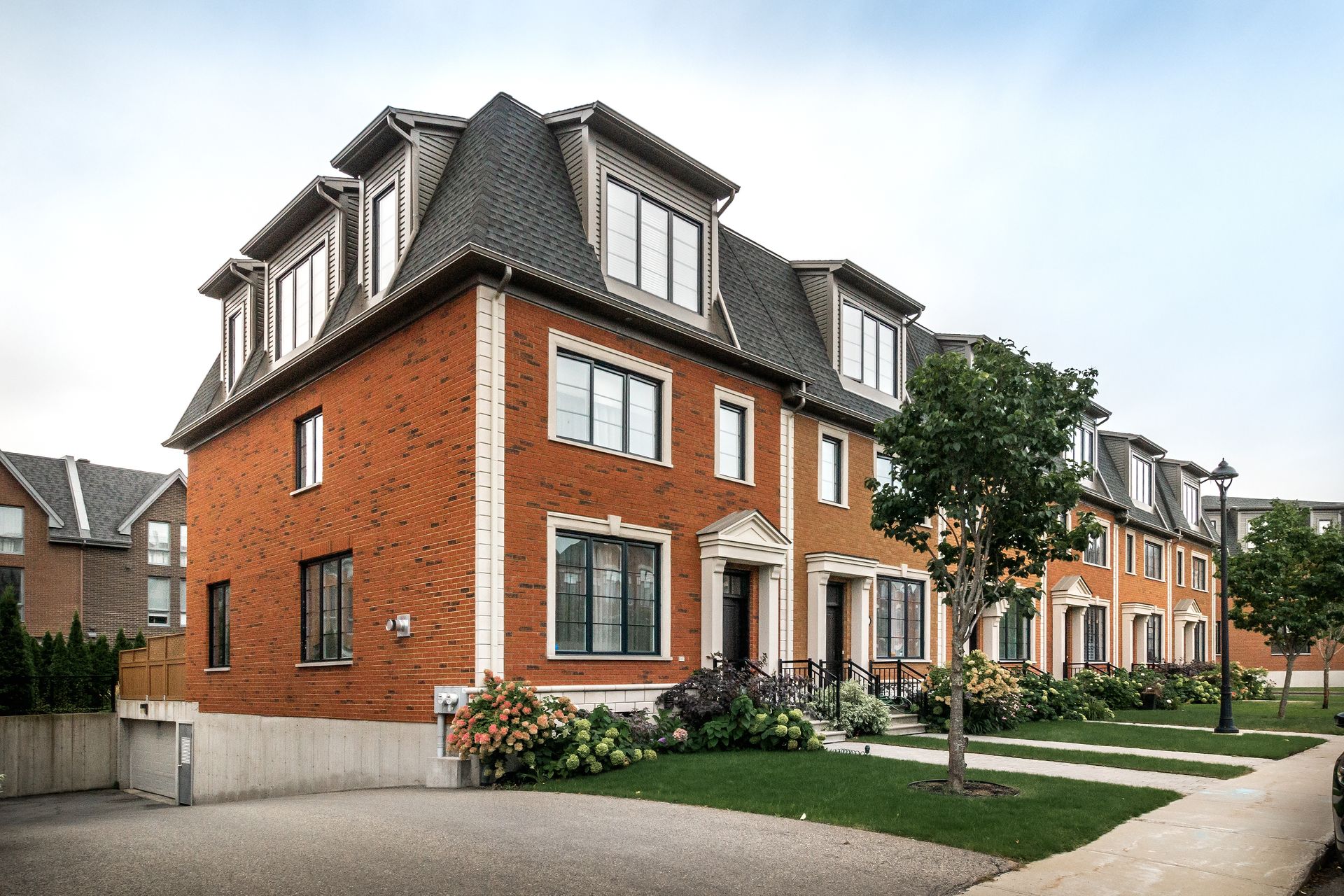 Modern brick townhouses with dark roofs and small front gardens along a quiet street