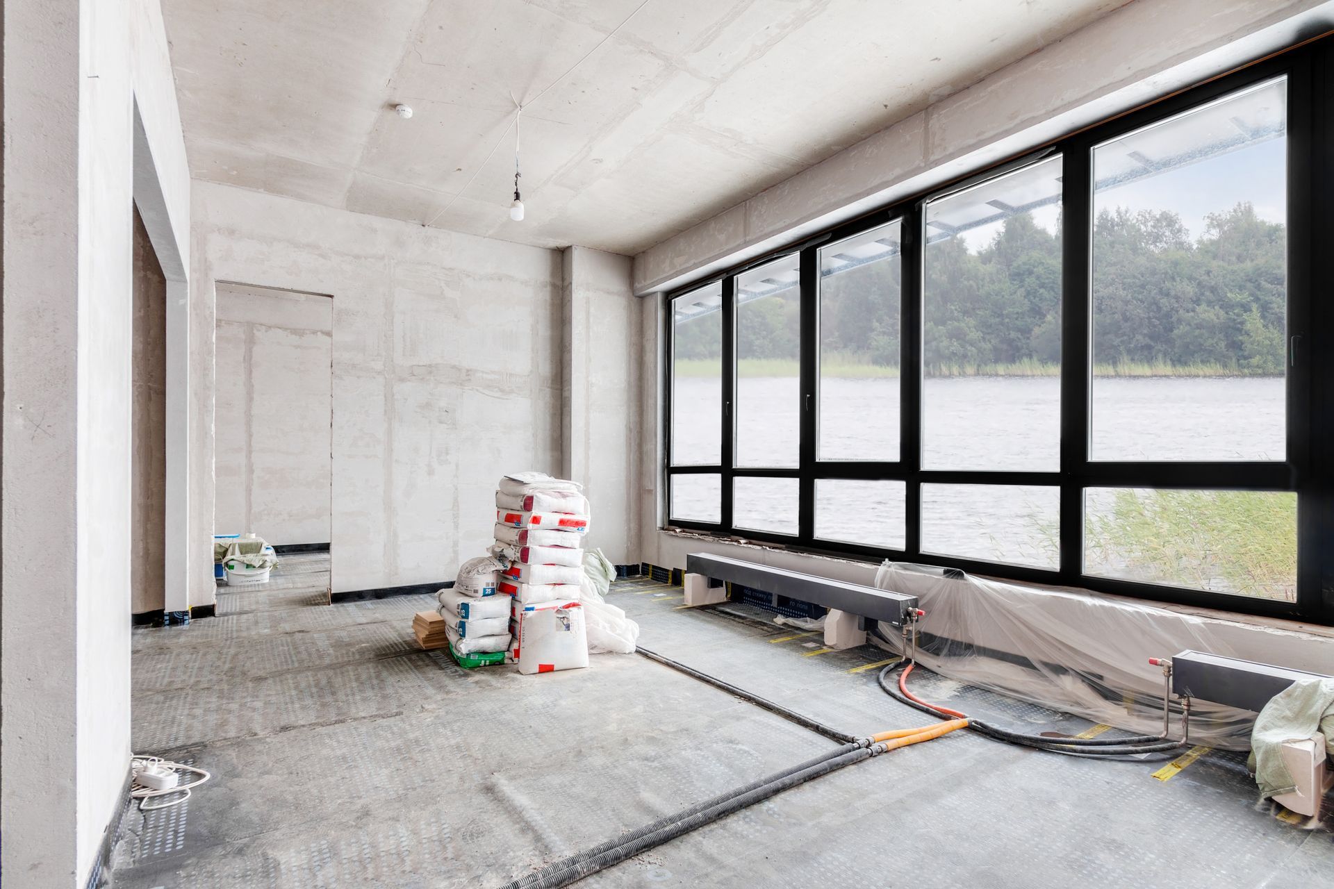 Unfinished room with large windows, construction materials, and tools on a concrete floor. Unfinished room with large windows, construction materials, and tools on a concrete floor.