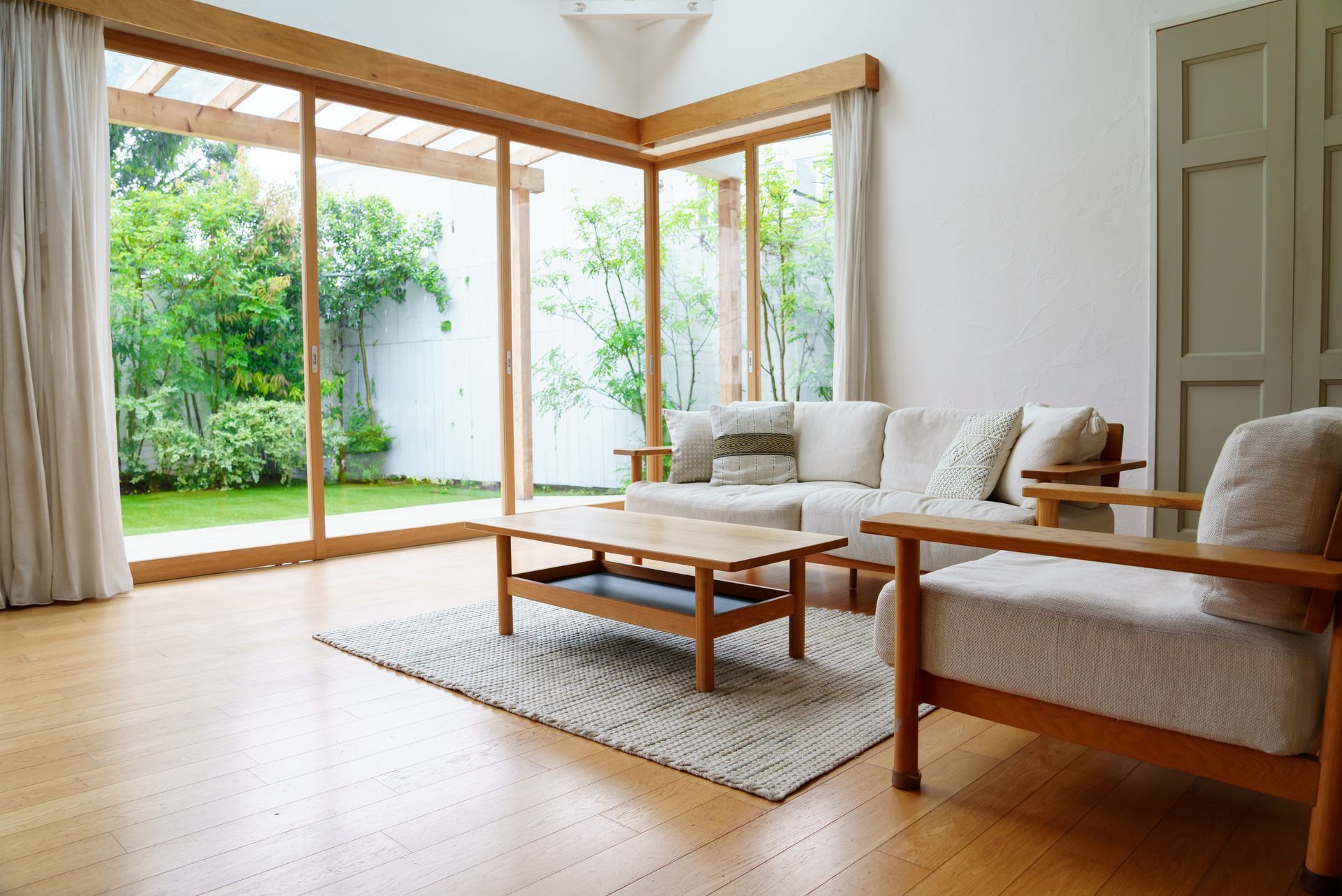 Bright living room with wooden furniture, rug, and large sliding doors opening to a green garden.