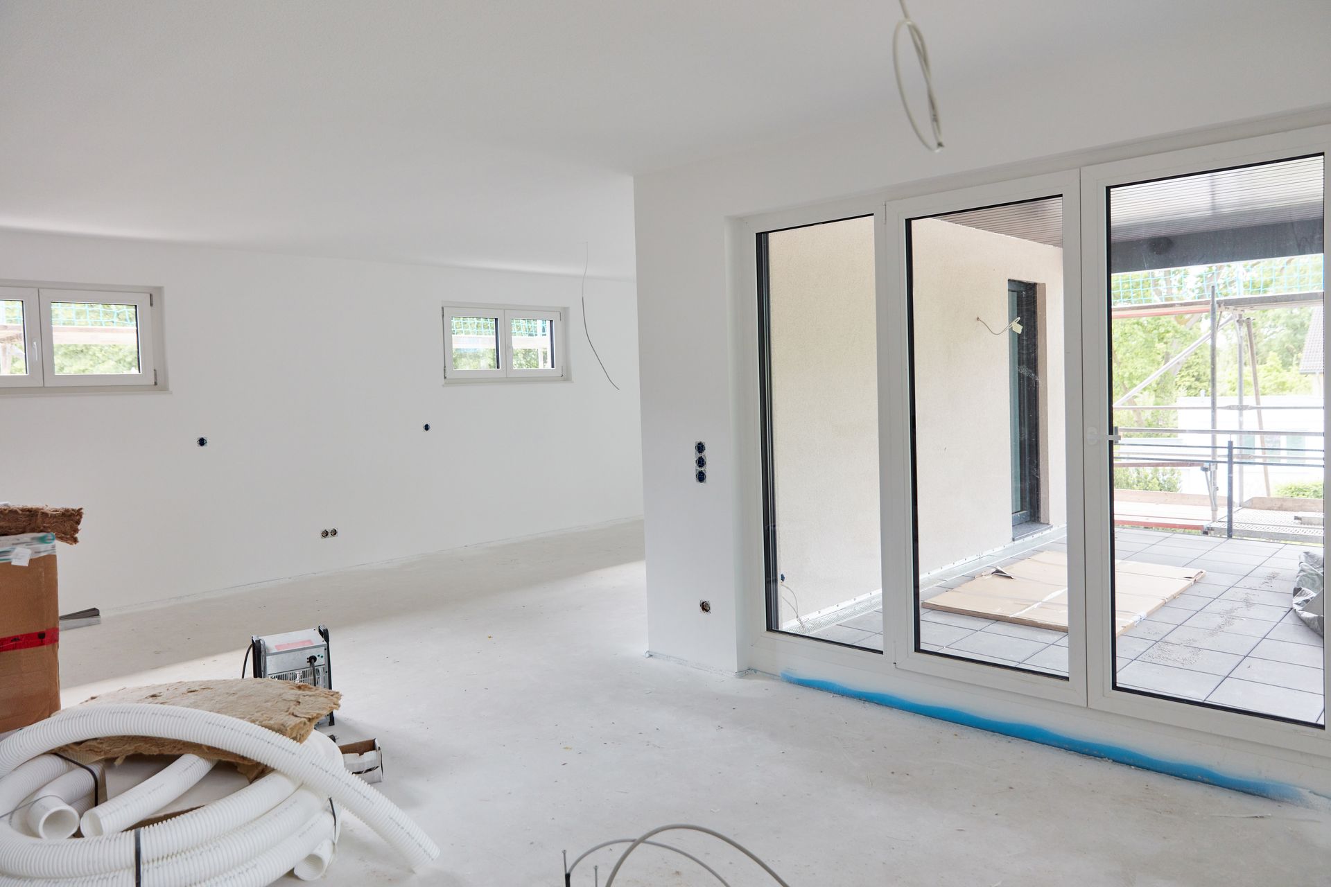 Bright unfinished room with white walls, sliding glass doors, and construction materials on the floor.