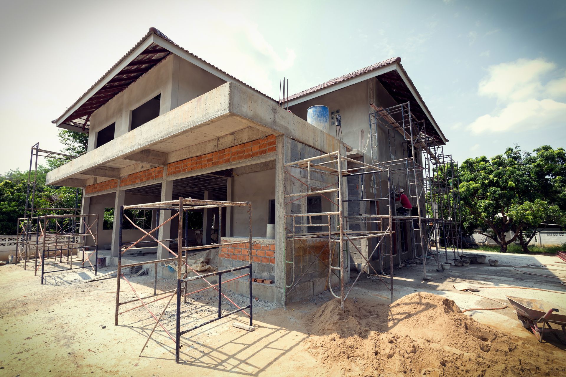 House under construction with scaffolding and unfinished exterior walls in a sandy yard.