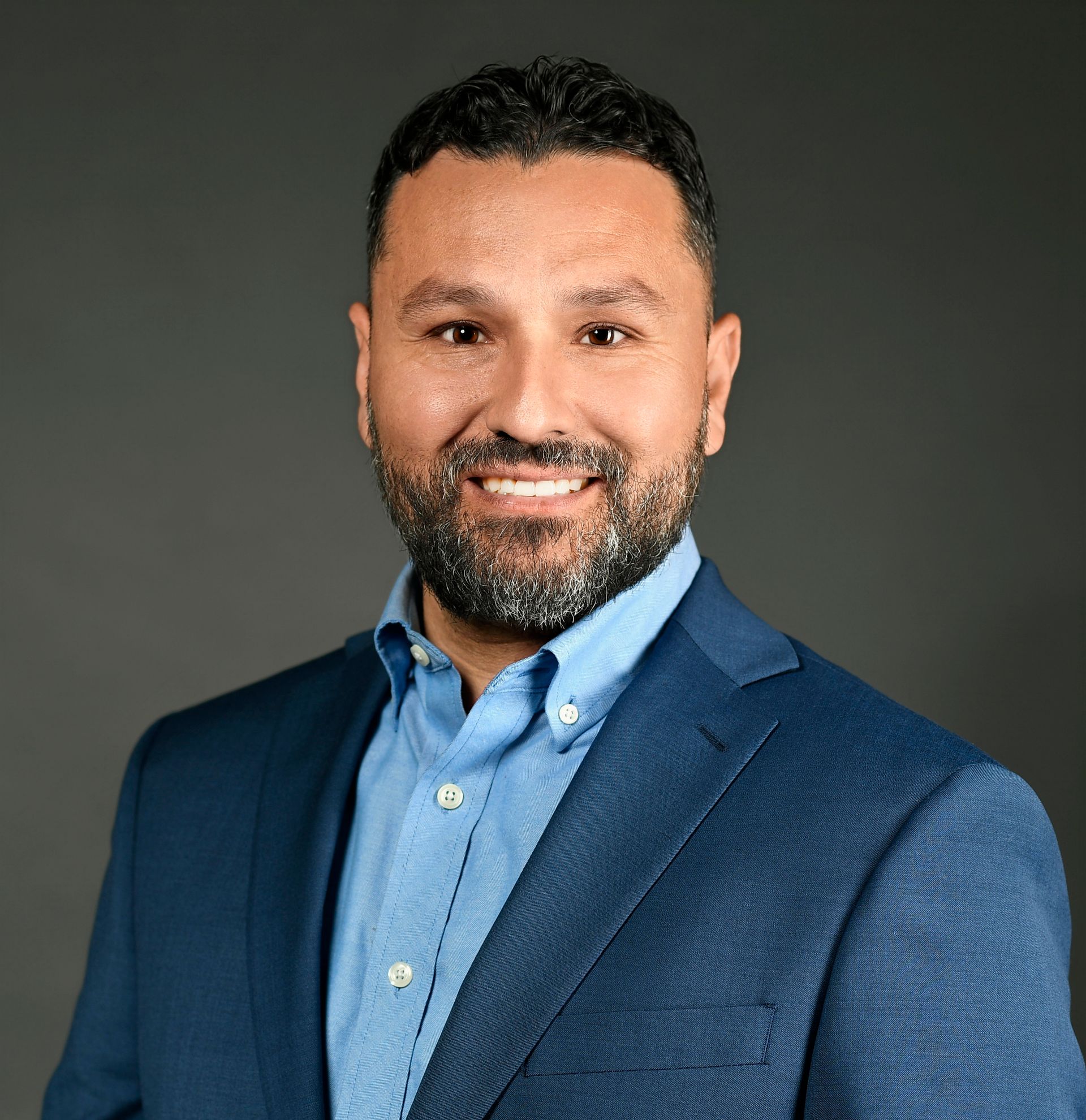 Smiling man in a blue blazer and shirt against a dark studio background