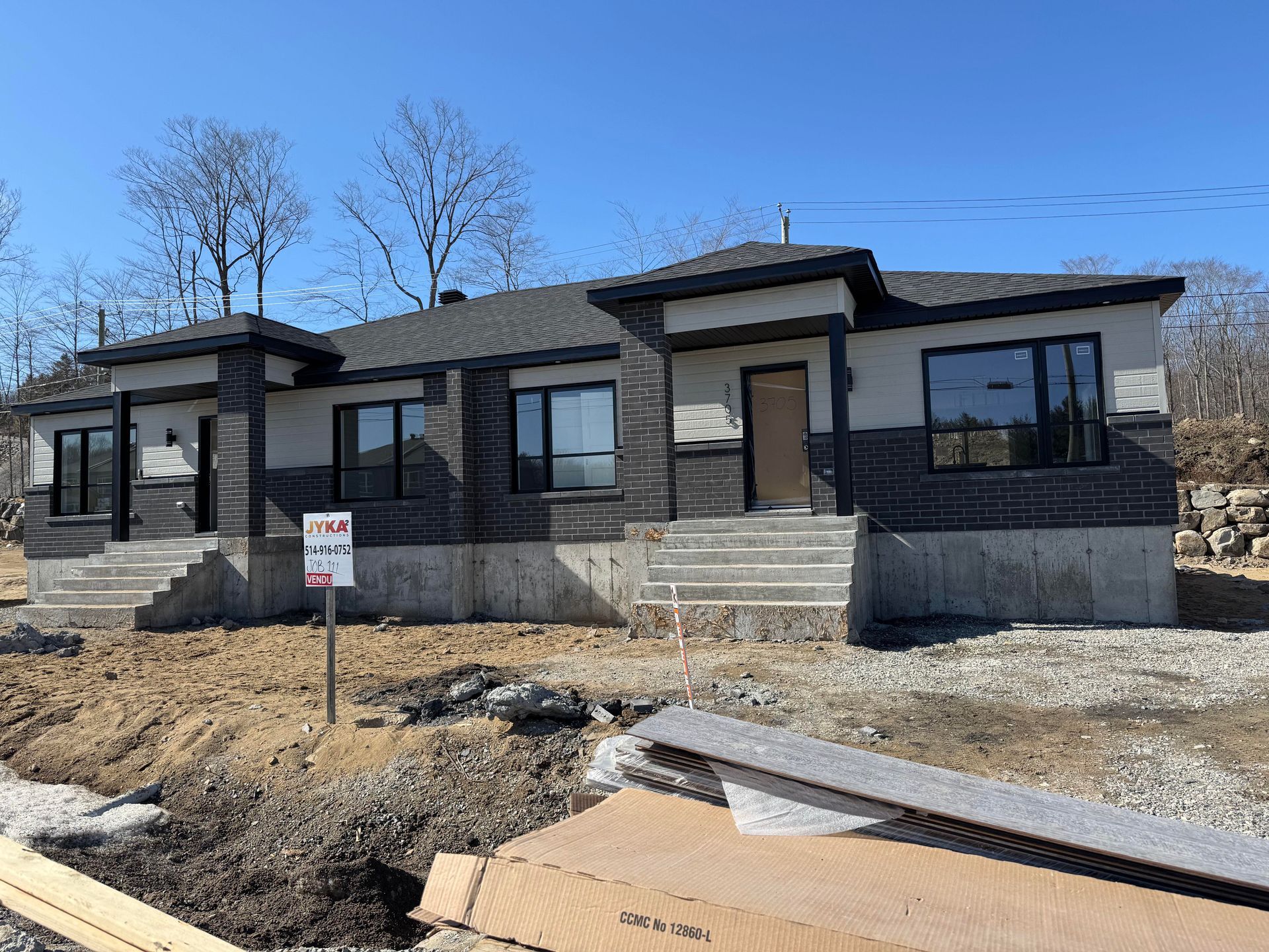 Nouvelle construction duplex avec des accents de briques foncées et une façade de couleur claire, sous un ciel bleu clair.