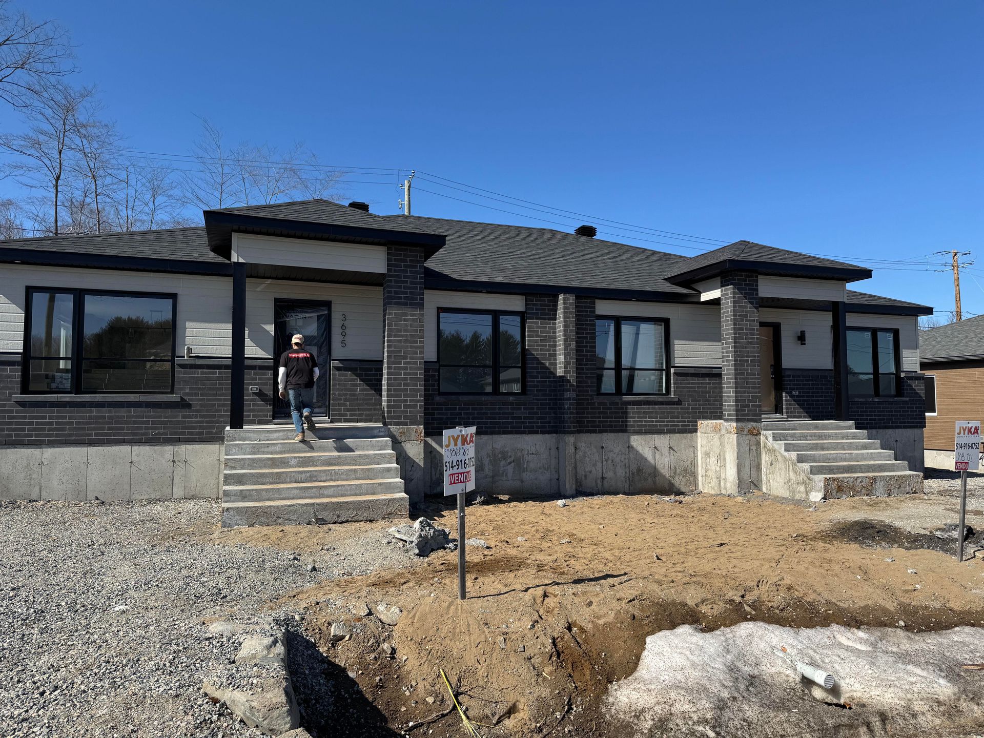 Nouvelle maison duplex en construction ; briques grises et noires, escaliers, ciel bleu.