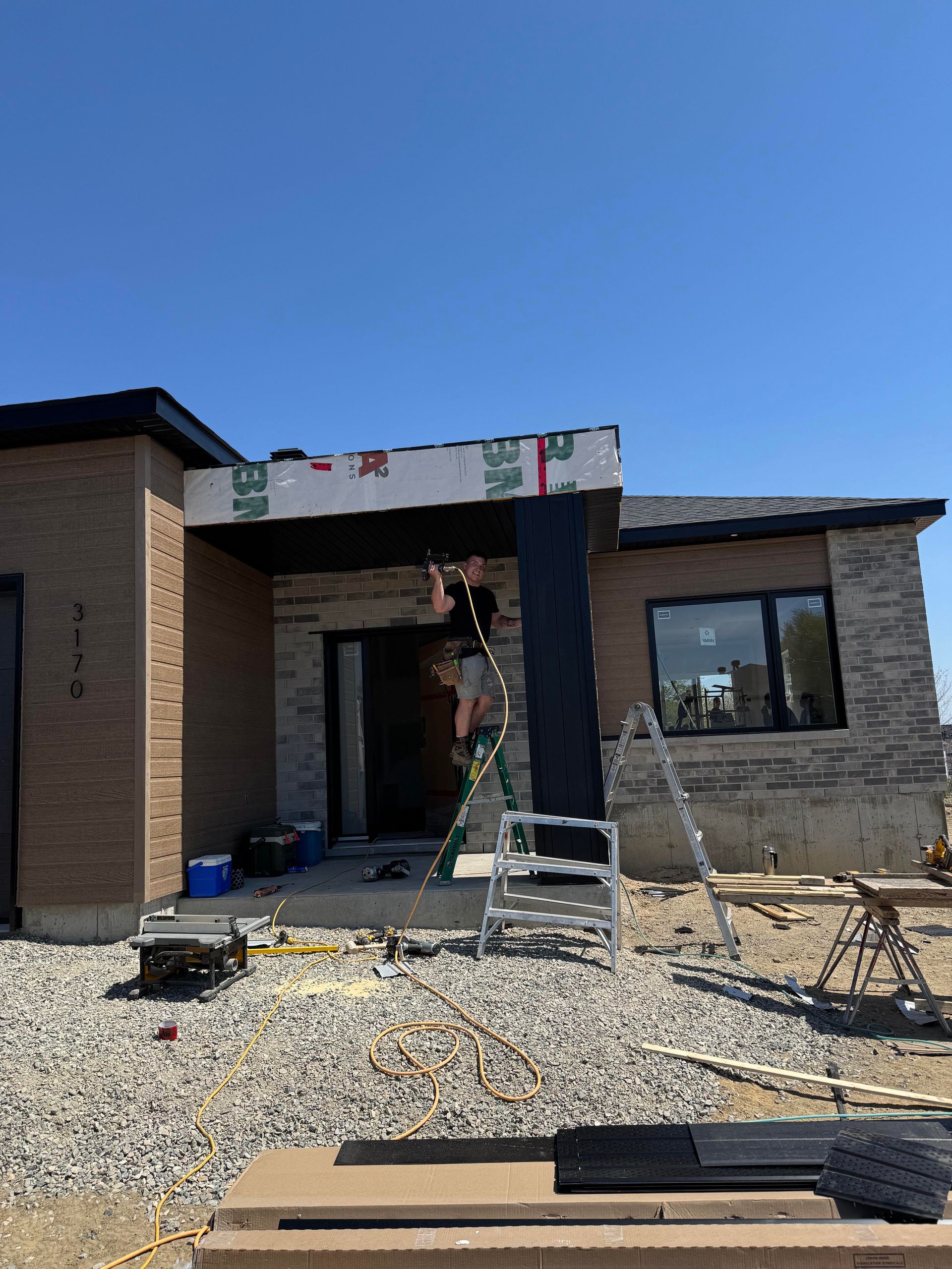 Un ouvrier du bâtiment pose un revêtement extérieur sur une maison neuve sous un ciel dégagé.
