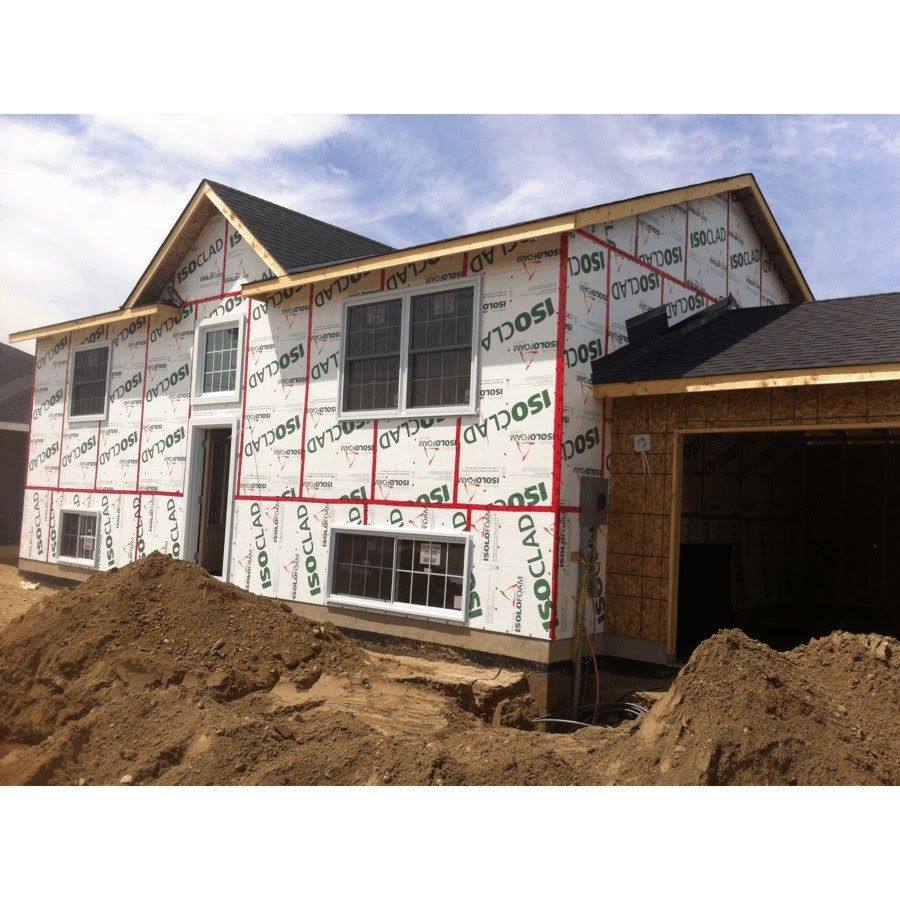 Maison en construction, recouverte d'une bâche blanche, avec charpente apparente et garage.