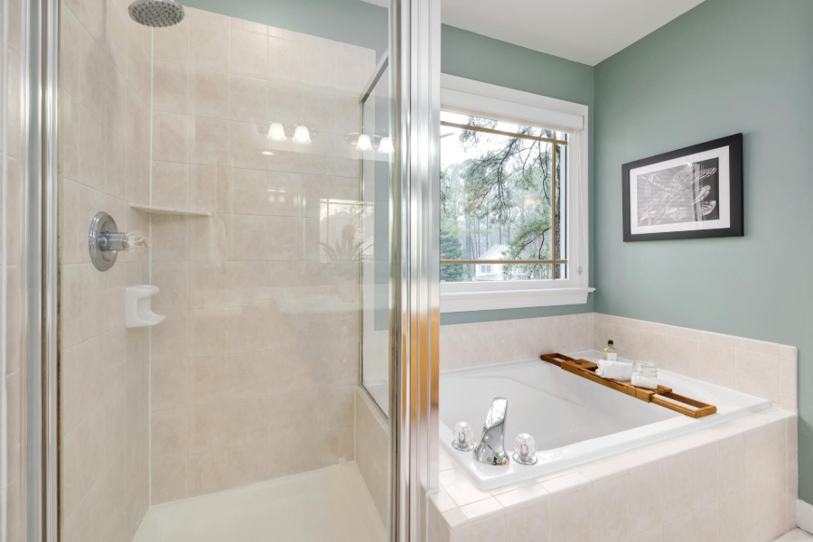 Modern bathroom with glass shower, white tub, and mint-green walls