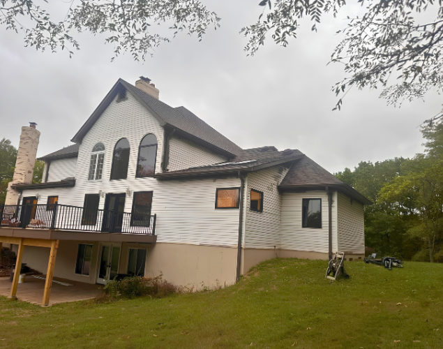 Two-story house with white siding, deck, and sloped grassy yard under cloudy sky