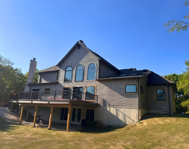 Two-story beige house with deck and large arched windows on a sunny lawn